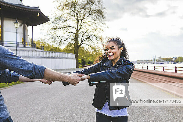 Glückliche junge Frau tanzt mit Freundin auf Fußweg im Park