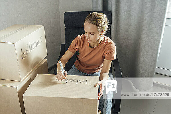 Woman writing with felt tip pen on cardboard box at home