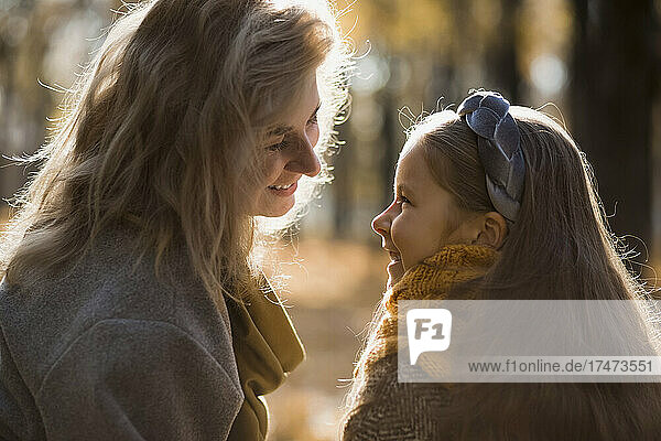Smiling mother and daughter sitting face to face in autumn park