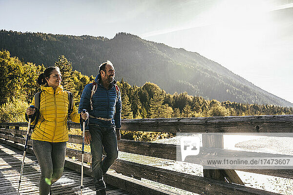 Smiling couple with hiking poles walking on bridge