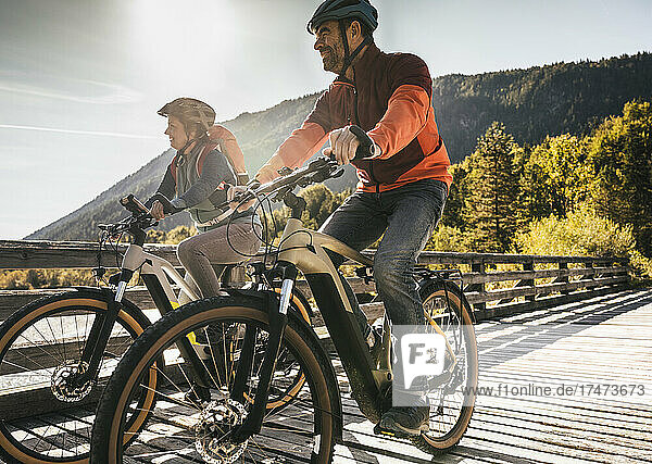 Smiling mature couple riding bicycles on bridge