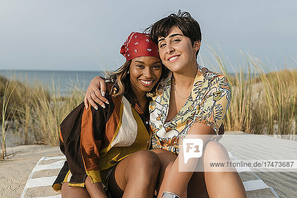 Smiling lesbian couple embracing each other sitting at beach