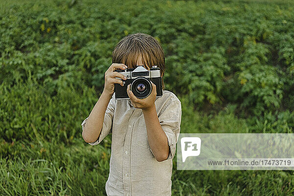 Boy photographing through vintage camera on field