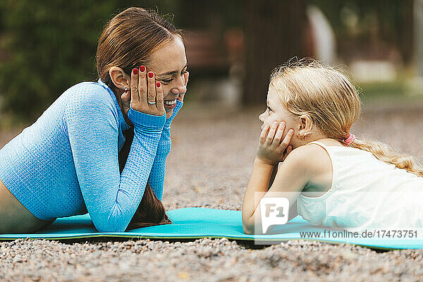 Smiling mother and daughter looking at each other while lying on exercise mat
