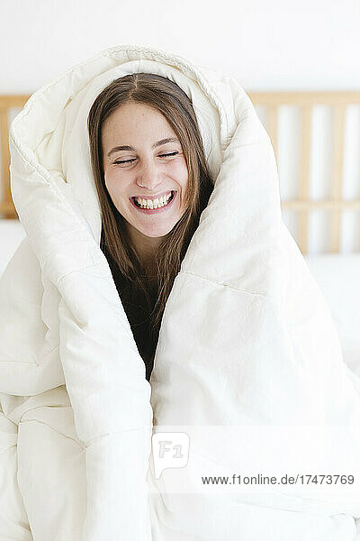 Happy young woman with eyes closed wrapped in blanket at home