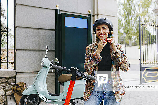 Smiling businesswoman with electric push scooter wearing helmet outside park