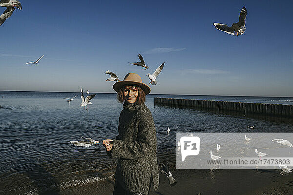 Smiling young woman feeding seagulls at sea
