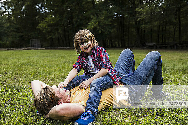 Boy playing with father lying on grass in park