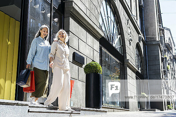 Mature women with shopping bags moving down from steps during sunny day