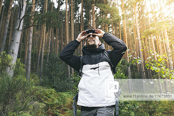 Male tourist looking through binoculars in forest