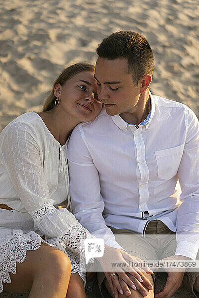 Young woman leaning over boyfriend's shoulder while sitting on sand