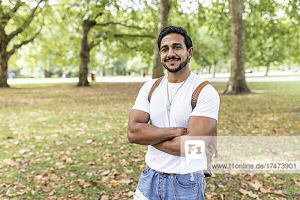 Smiling young man standing with arms crossed in park