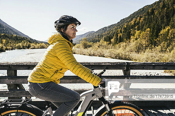 Woman with crash helmet riding mountain bike on sunny day