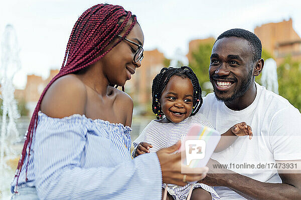 Smiling man with daughter looking at woman showing smart phone