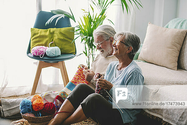 Smiling senior couple knitting wool together at home