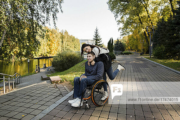Woman embracing disabled man on wheelchair from behind
