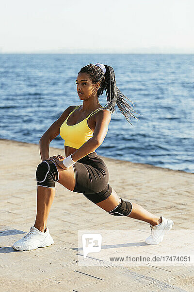 Young female athlete doing stretching exercise near sea