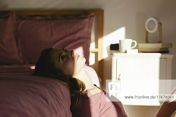 Young woman in depression leaning on bed in bedroom