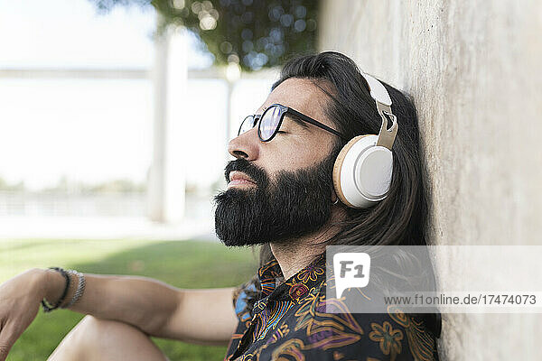 Bearded man with eyes closed listening music in public park