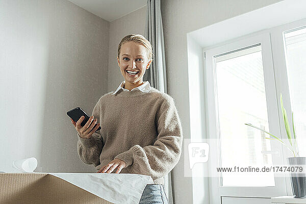 Happy woman with mobile phone and plan in new apartment