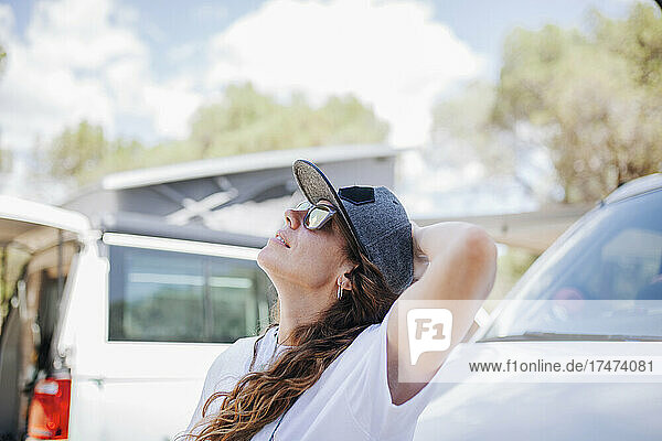 Woman wearing cap and sunglasses looking up by camper van