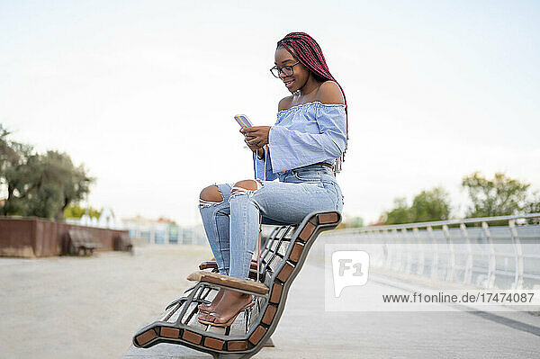 Young woman text messaging through mobile phone on bench