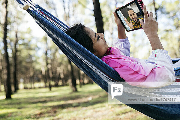 Young woman on video call through digital tablet in hammock