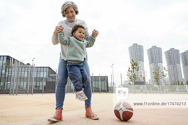 Grandmother lifting granddaughter on sports field