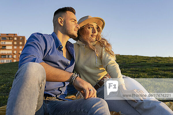 Young couple sitting together on hill at sunset