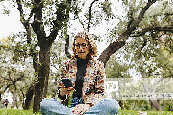 Businesswoman wearing eyeglasses using mobile phone in park