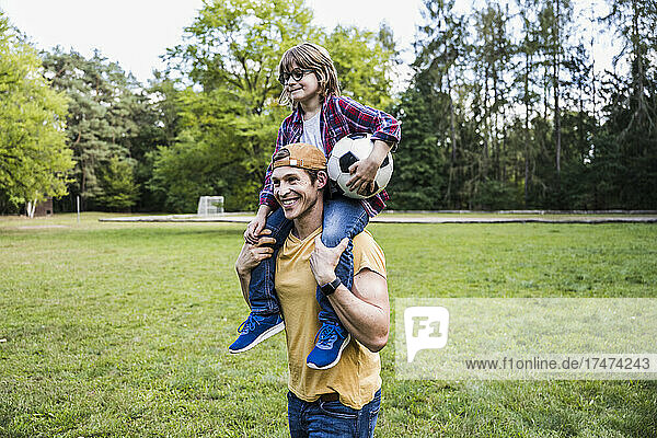 Smiling father carrying son on shoulders at park