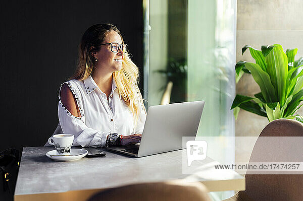 Smiling businesswoman looking out of window while working in coffee shop