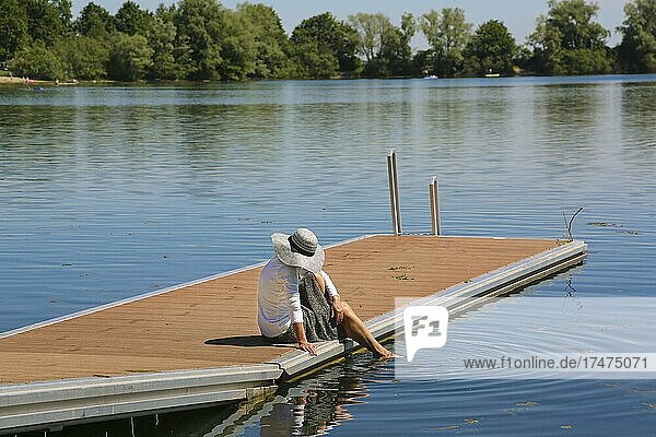 Frau mit Sonnenhut auf Steg  ein Bein im Wasser  Ludwigsfelder See  Badesee  Gewässer  Neu-Ulm  Bayern  Deutschland  Europa