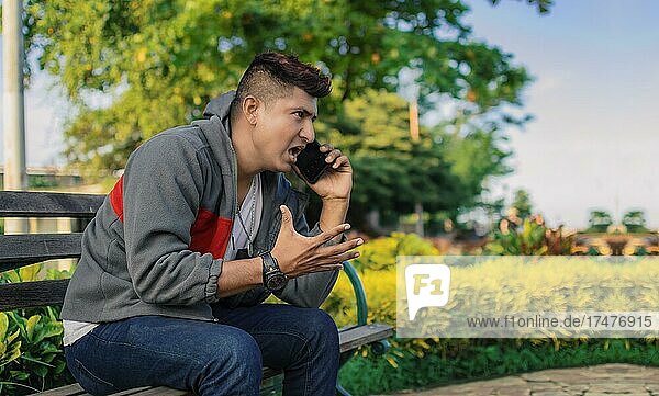 Man sitting on a bench calling on the phone  young man calling on the cell phone  angry man calling on the phone in a park