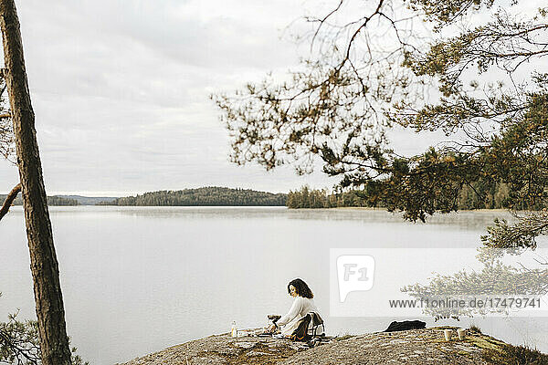 Junge Frau sitzt auf einem Felsen am Seeufer