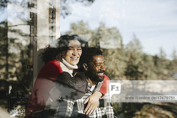 Porträt einer fröhlichen Frau  die ihren Freund umarmt  gesehen durch ein Fenster