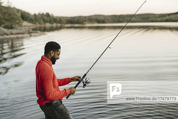 Lächelnder Mann beim Fischen im See während des Sonnenuntergangs
