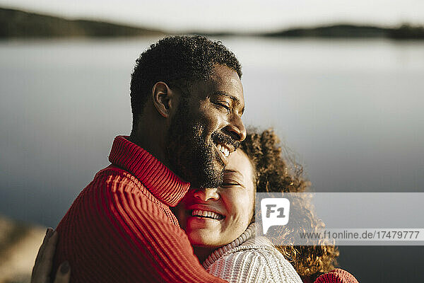Happy couple embracing by lake on sunny day