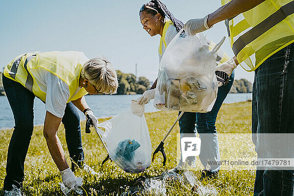 Männliche und weibliche Freiwillige reinigen an einem sonnigen Tag Plastik am Seeufer