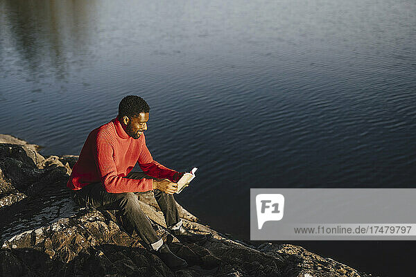 Mann  der am Wochenende auf einem Felsen sitzend ein Buch liest
