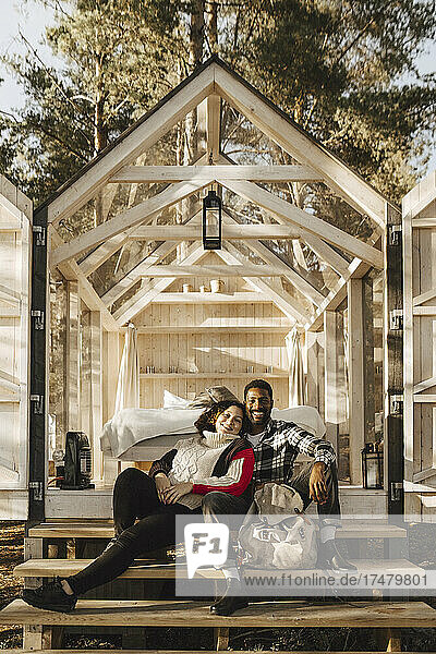 Ganzes Porträt eines lächelnden Paares  das auf den Stufen einer Hütte sitzt