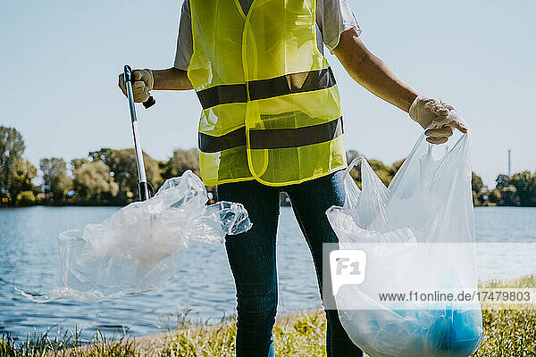 Mittelteil eines jungen männlichen Umweltschützers  der am See Plastik aufhebt