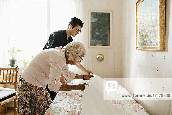 Senior woman and male healthcare worker placing blanket on bed at home