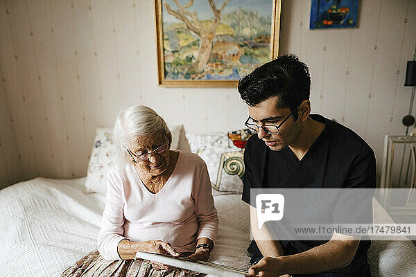 Junger Krankenpfleger zeigt einer älteren Frau  die zu Hause auf dem Bett sitzt  einen Spiegel