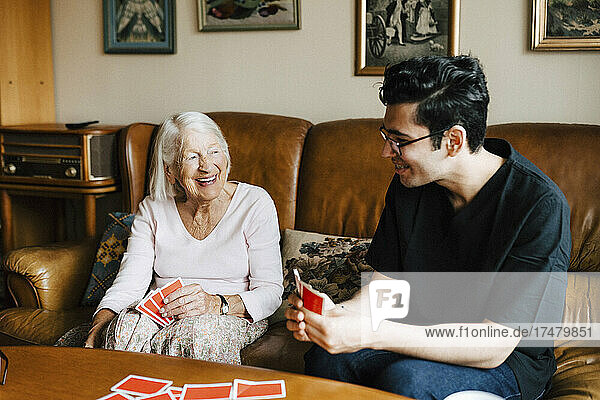 Happy male healthcare worker playing cards with elderly woman in living room