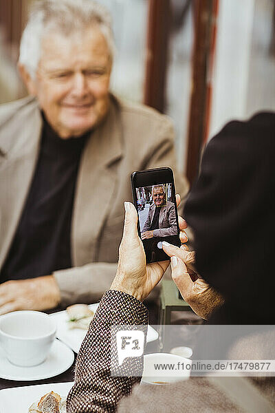 Frau fotografiert älteren Mann mit Smartphone in einem Straßencafé