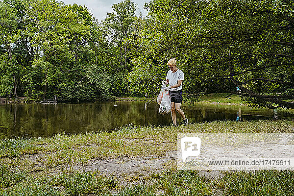 Junger männlicher Freiwilliger reinigt Plastikmüll am Teich