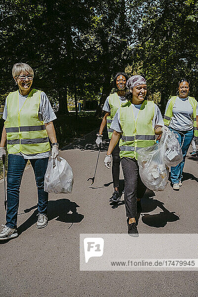 Multirassische weibliche Freiwillige mit Plastiktüten  die an einem sonnigen Tag im Park spazieren gehen