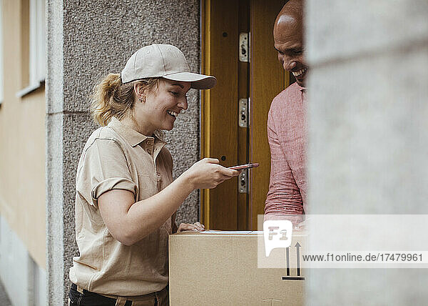 Eine lächelnde Mitarbeiterin fotografiert ein Paket bei der Auslieferung an einen männlichen Kunden