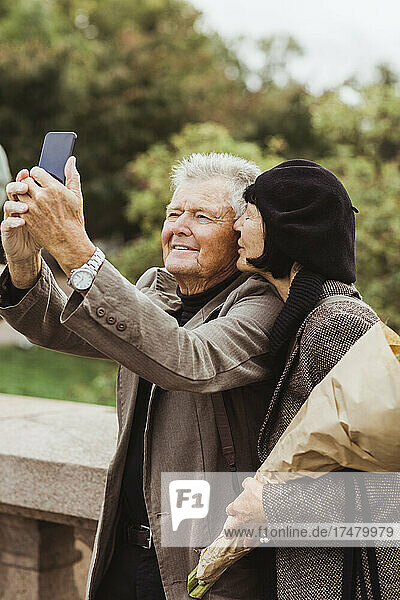 Frau küsst älteren Mann  der am Wochenende ein Selfie mit seinem Smartphone macht